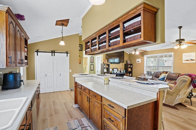 kitchen with a barn door, open floor plan, hanging light fixtures, crown molding, and light wood-style floors