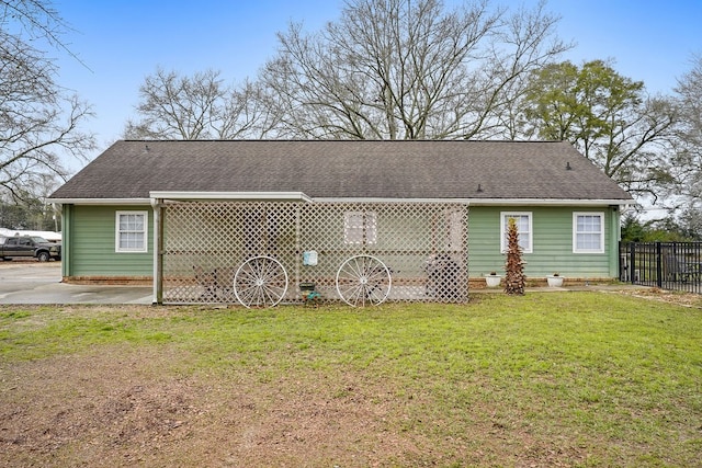 rear view of property featuring a shingled roof, a yard, and fence