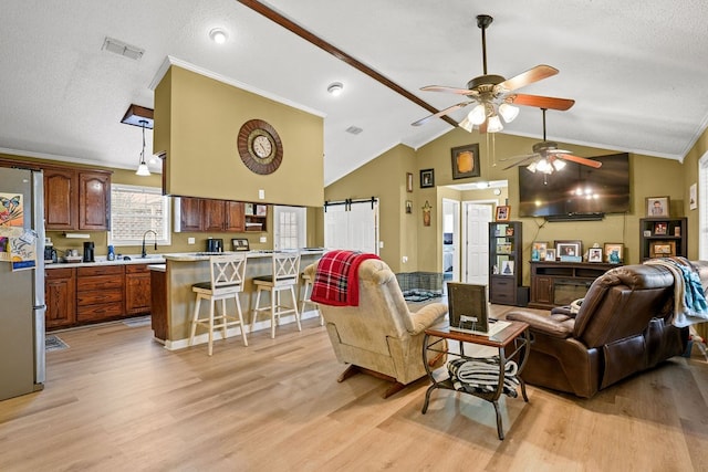 living area featuring a textured ceiling, lofted ceiling, a barn door, visible vents, and light wood finished floors