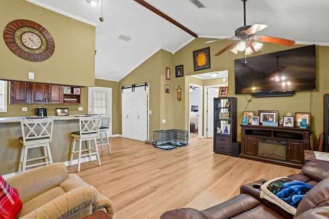 living area featuring lofted ceiling, a barn door, a ceiling fan, ornamental molding, and light wood finished floors