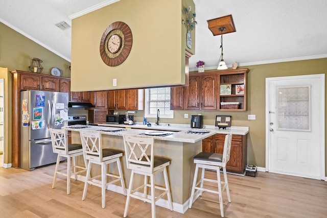 kitchen with visible vents, a breakfast bar area, freestanding refrigerator, light countertops, and under cabinet range hood