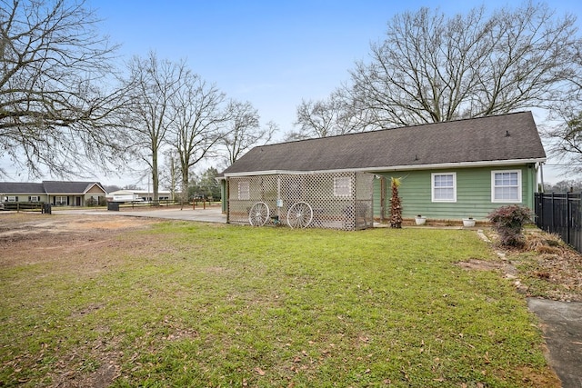 rear view of house featuring roof with shingles, a lawn, and fence