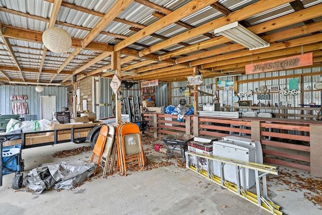 miscellaneous room featuring a workshop area, metal wall, and unfinished concrete flooring