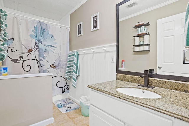 bathroom with tile patterned flooring, vanity, visible vents, ornamental molding, and wainscoting