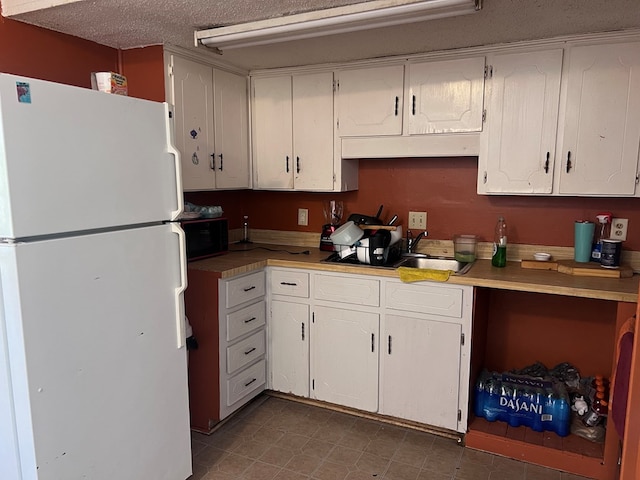 kitchen featuring white refrigerator, white cabinetry, and a textured ceiling