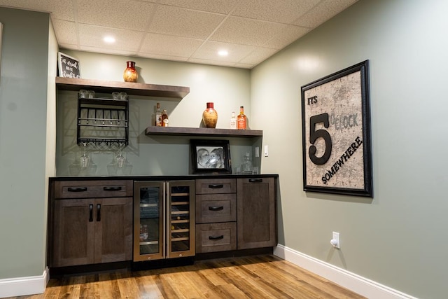 bar with wine cooler, dark brown cabinetry, hardwood / wood-style floors, and a paneled ceiling