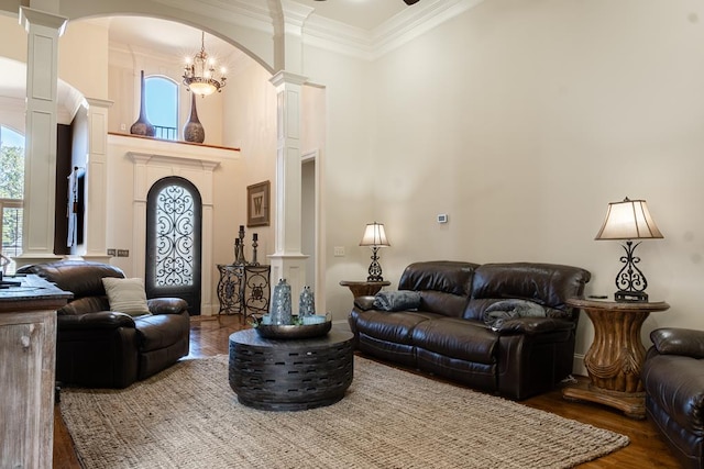 living room featuring a high ceiling, dark hardwood / wood-style floors, ornate columns, ornamental molding, and a notable chandelier