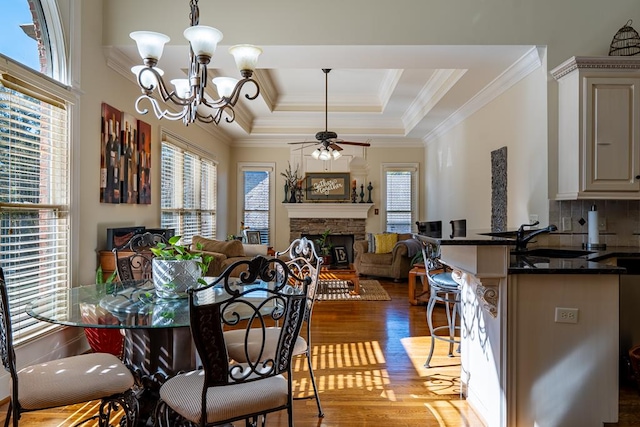 dining area featuring ceiling fan with notable chandelier, crown molding, sink, light hardwood / wood-style flooring, and a stone fireplace