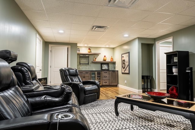 living room with indoor bar, light hardwood / wood-style floors, a drop ceiling, and beverage cooler