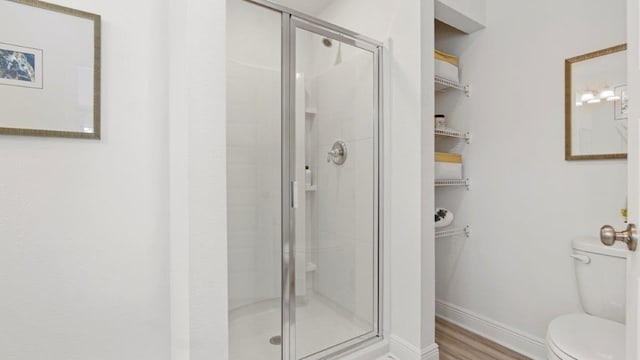 bathroom with a stall shower, baseboards, toilet, and wood finished floors