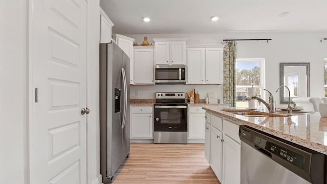 kitchen featuring a sink, stainless steel appliances, white cabinets, light wood-type flooring, and light stone counters
