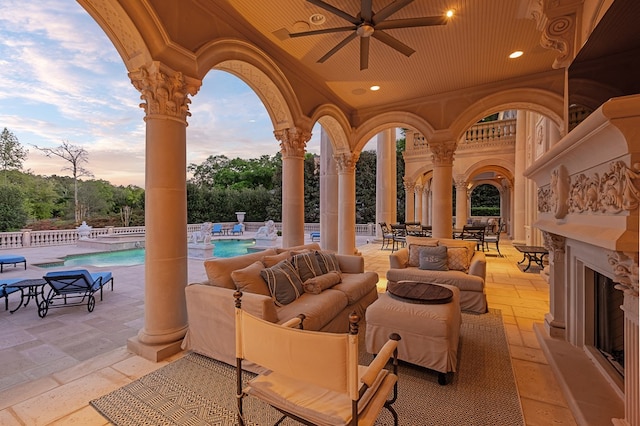 patio terrace at dusk featuring an outdoor living space with a fireplace, ceiling fan, and a community pool