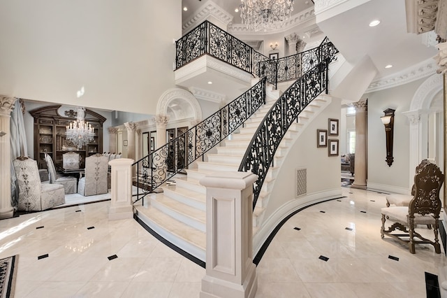 stairway featuring a towering ceiling, decorative columns, and an inviting chandelier