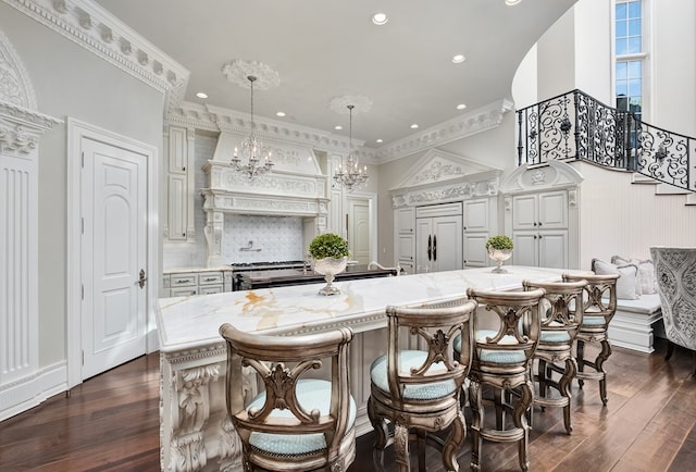 kitchen with ornamental molding, dark wood-type flooring, paneled built in refrigerator, pendant lighting, and a breakfast bar area