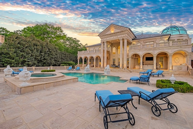 pool at dusk with an in ground hot tub and a patio