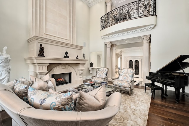 living room with dark hardwood / wood-style flooring, a towering ceiling, ornamental molding, and ornate columns