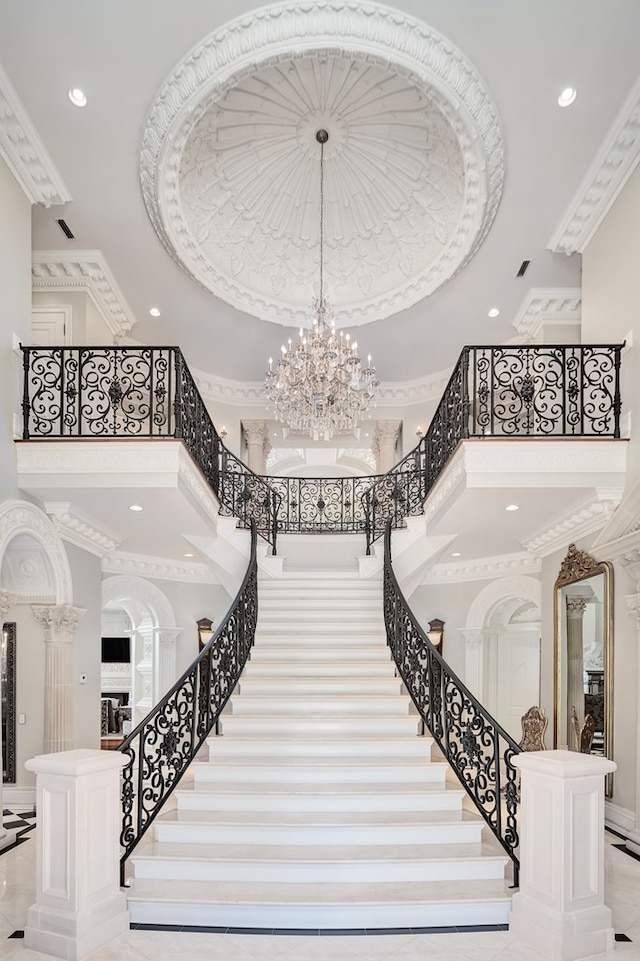 staircase featuring crown molding, a chandelier, and a high ceiling