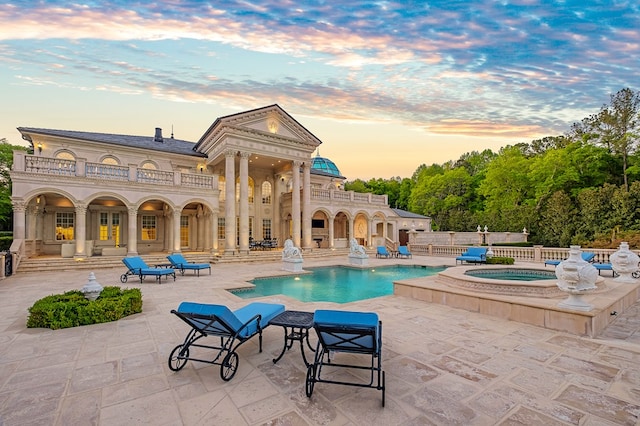 pool at dusk featuring an in ground hot tub and a patio