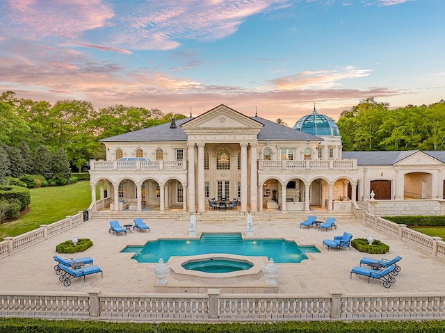 back house at dusk with a pool with hot tub, a patio area, and a balcony