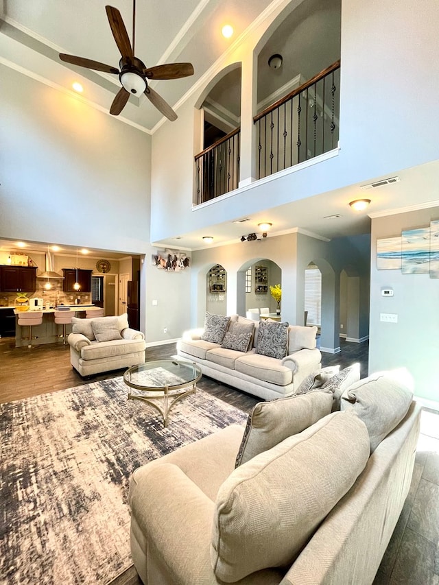 living room with dark wood finished floors, arched walkways, a ceiling fan, and ornamental molding