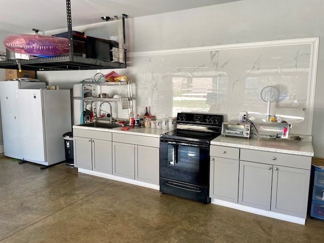 kitchen featuring black electric range, a sink, finished concrete floors, freestanding refrigerator, and light countertops