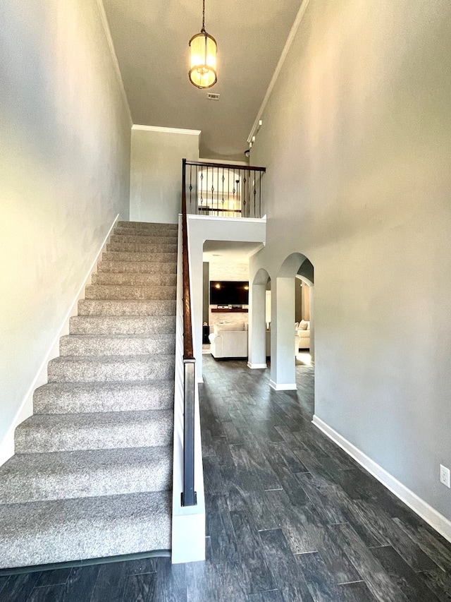 stairway featuring crown molding, baseboards, a high ceiling, wood finished floors, and arched walkways