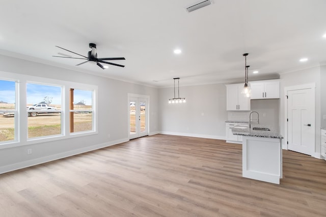 kitchen with pendant lighting, crown molding, dark stone countertops, white cabinetry, and a center island with sink