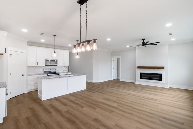 kitchen featuring pendant lighting, appliances with stainless steel finishes, a kitchen island with sink, light stone countertops, and white cabinets