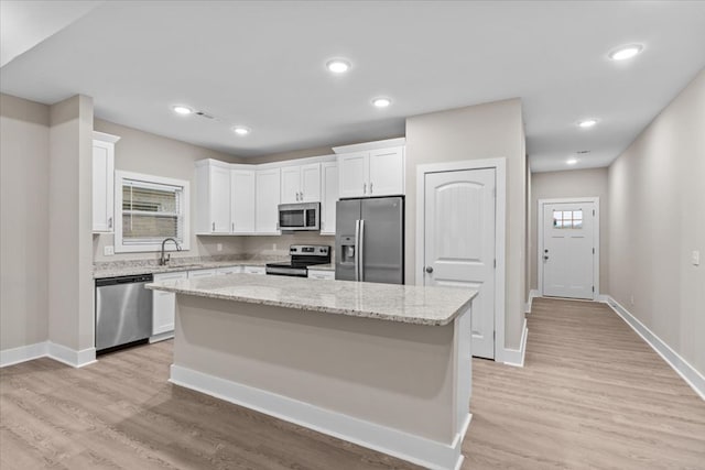 kitchen with appliances with stainless steel finishes, light stone counters, sink, white cabinets, and a center island