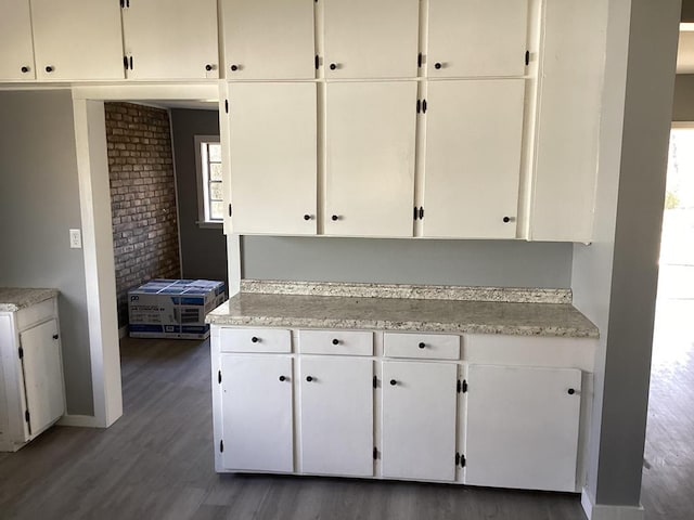 kitchen featuring wood finished floors, baseboards, brick wall, light countertops, and white cabinets