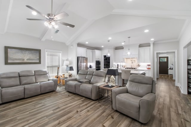 living room with ceiling fan, sink, vaulted ceiling with beams, light hardwood / wood-style flooring, and ornamental molding