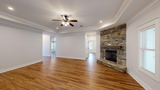 unfurnished living room featuring a stone fireplace, ceiling fan, ornamental molding, and hardwood / wood-style flooring