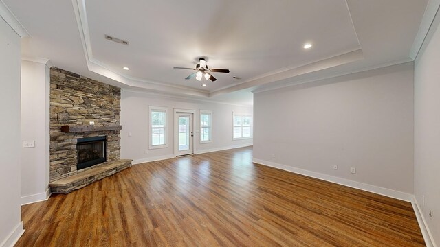 unfurnished living room with ornamental molding, a tray ceiling, ceiling fan, wood-type flooring, and a fireplace