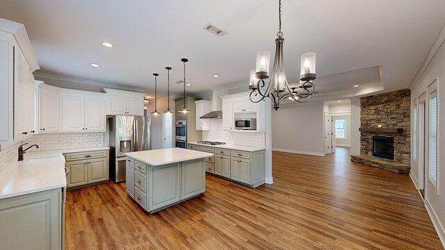 kitchen with stainless steel appliances, sink, pendant lighting, a kitchen island, and a stone fireplace