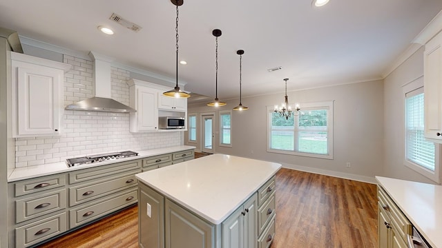 kitchen featuring a center island, wall chimney range hood, hardwood / wood-style floors, decorative light fixtures, and appliances with stainless steel finishes