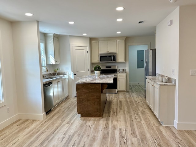 kitchen with sink, light stone countertops, light wood-type flooring, cream cabinetry, and stainless steel appliances