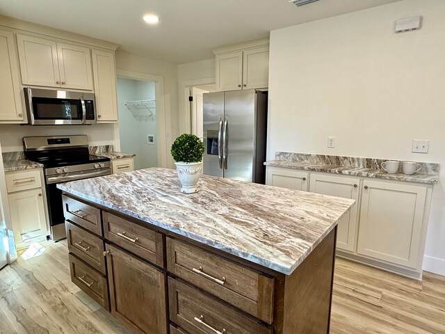 kitchen with light stone counters, a center island, stainless steel appliances, and light hardwood / wood-style floors