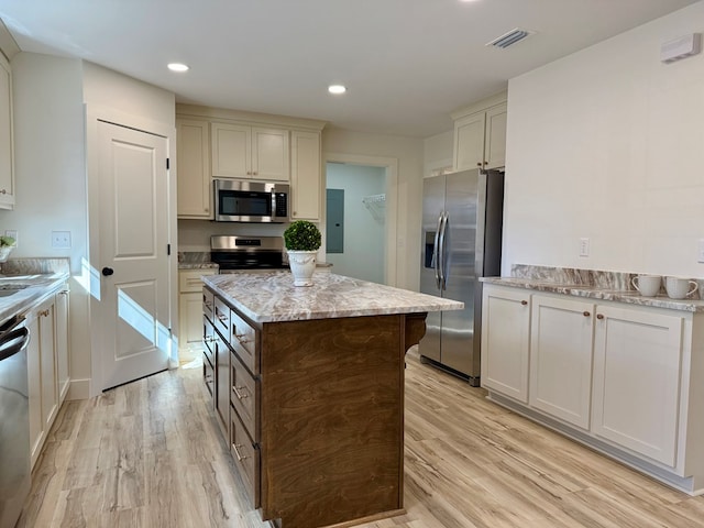 kitchen with a center island, electric panel, light stone countertops, appliances with stainless steel finishes, and light hardwood / wood-style floors