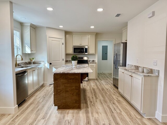 kitchen with a center island, sink, light stone countertops, appliances with stainless steel finishes, and light hardwood / wood-style floors