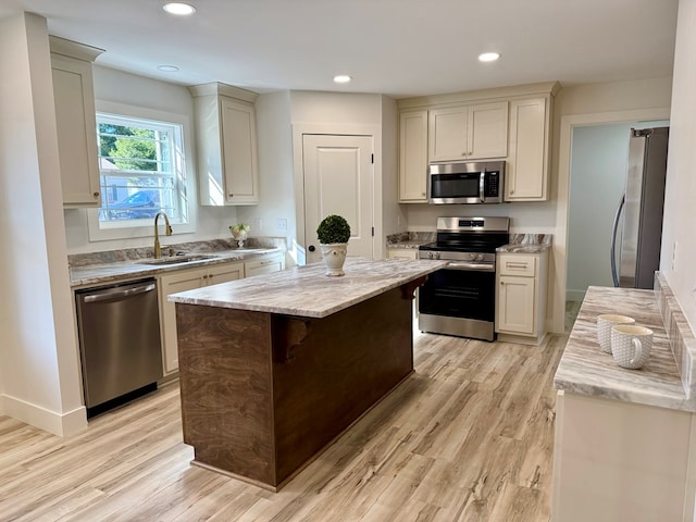 kitchen with sink, light stone counters, appliances with stainless steel finishes, a kitchen island, and light wood-type flooring