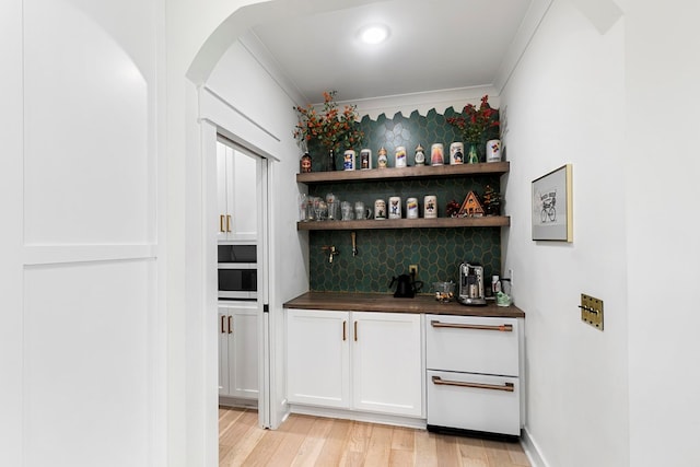 481 Grace Dr, Newton, AL 36352 - indoor wet bar featuring decorative backsplash, crown molding, arched walkways, stainless steel microwave, and light wood finished floors