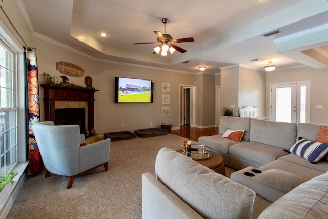 living room featuring ceiling fan, visible vents, a tiled fireplace, crown molding, and a tray ceiling