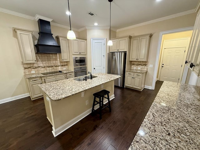 kitchen with pendant lighting, light stone counters, black appliances, custom range hood, and an island with sink