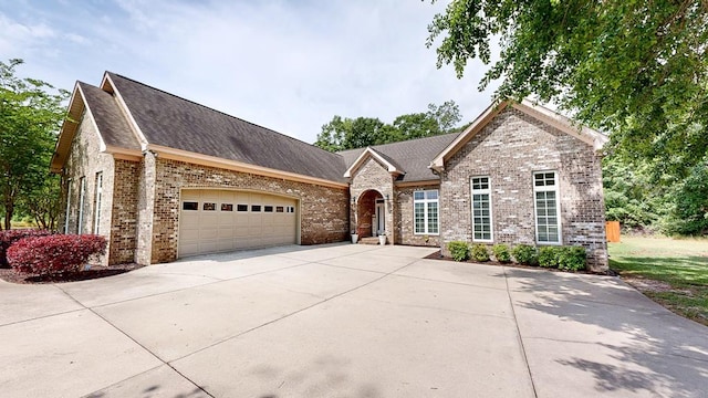 view of front facade with driveway, brick siding, roof with shingles, and a garage