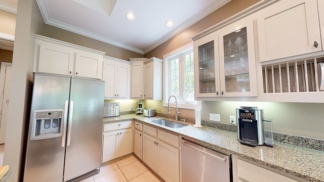 kitchen with light stone counters, stainless steel appliances, a sink, crown molding, and glass insert cabinets