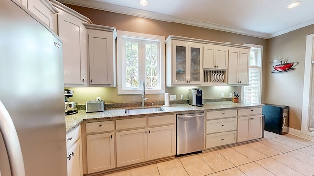 kitchen featuring stainless steel appliances, light tile patterned floors, a sink, crown molding, and glass insert cabinets