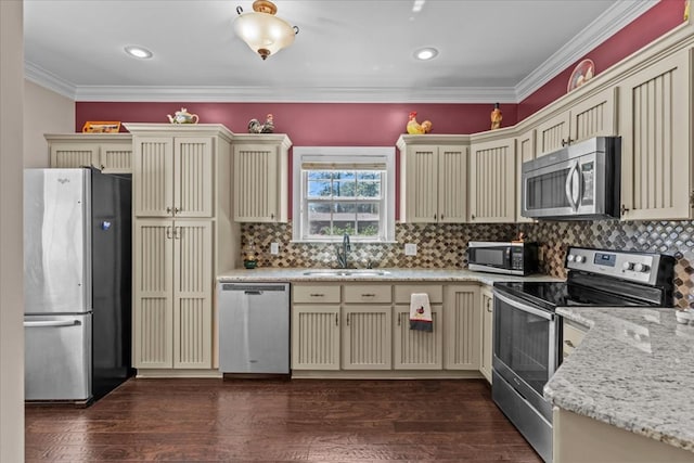 kitchen featuring crown molding, a sink, appliances with stainless steel finishes, cream cabinetry, and dark wood-type flooring
