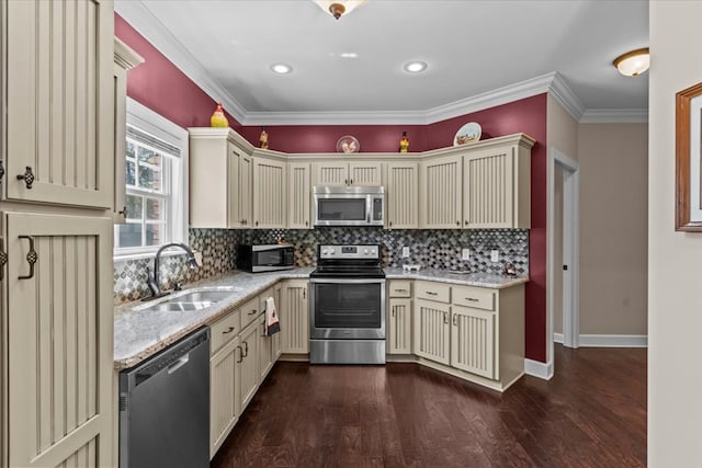 kitchen with a sink, light stone countertops, appliances with stainless steel finishes, cream cabinets, and dark wood-type flooring
