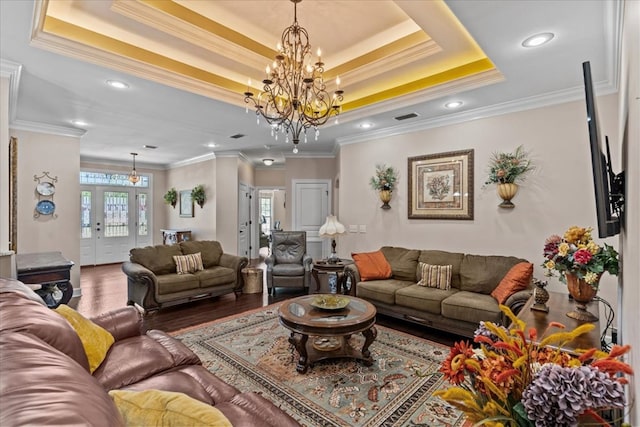 living area with visible vents, ornamental molding, wood finished floors, a raised ceiling, and a notable chandelier