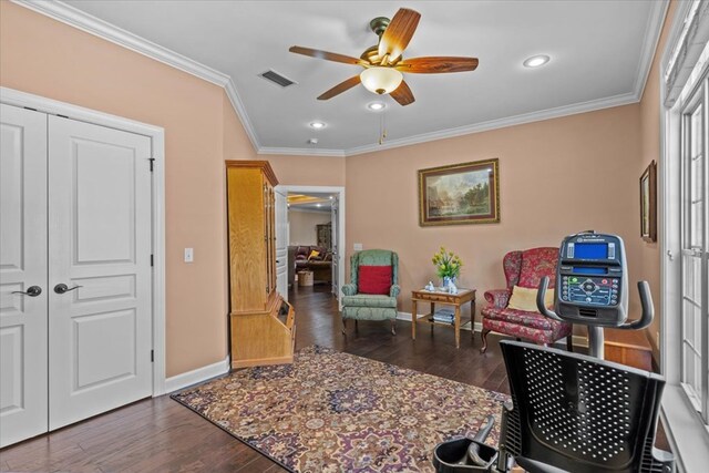 living area with a ceiling fan, wood finished floors, baseboards, visible vents, and ornamental molding